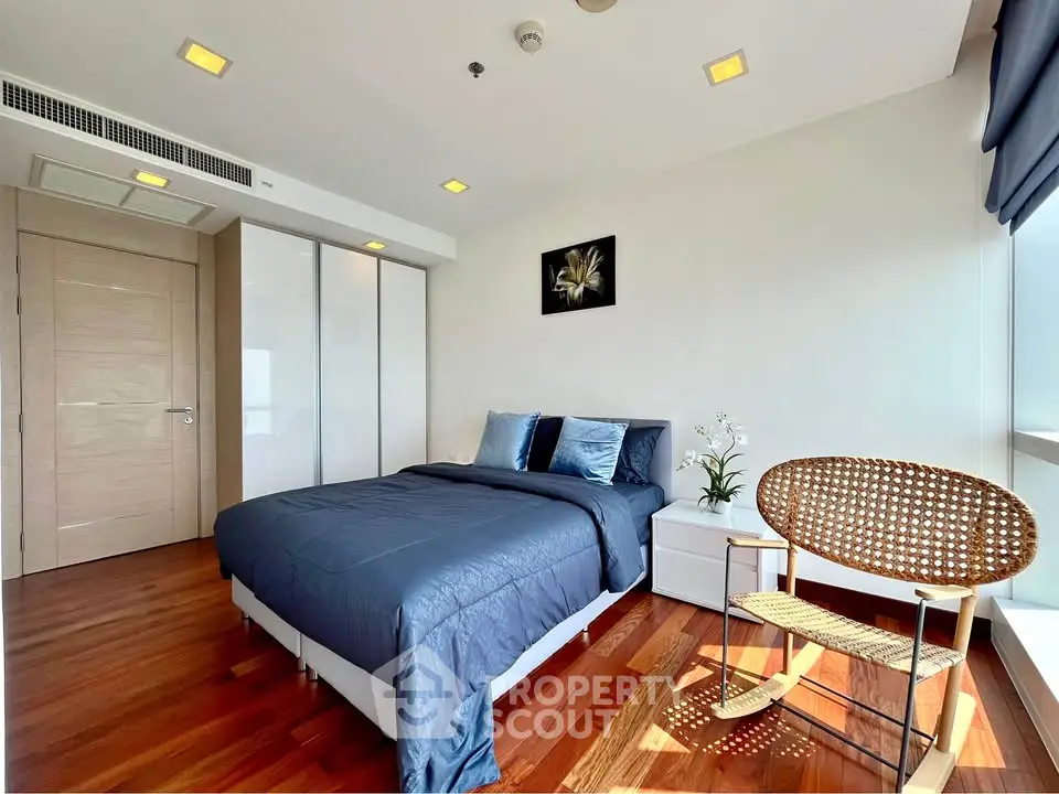 Modern bedroom with wooden flooring and stylish decor, featuring a cozy bed and natural light.