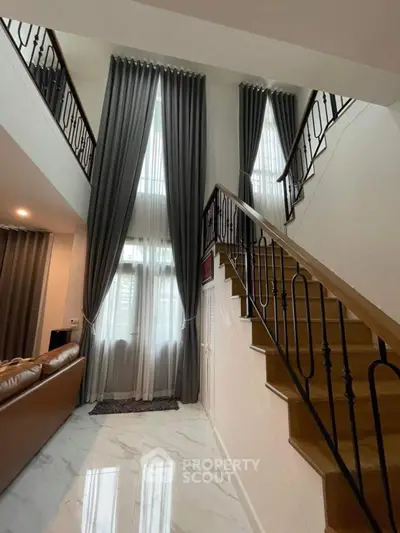 Elegant high-ceiling living room with grand staircase and luxurious curtains