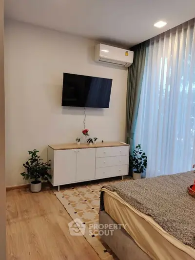 Modern bedroom with wall-mounted TV and air conditioning, featuring stylish decor and natural light.