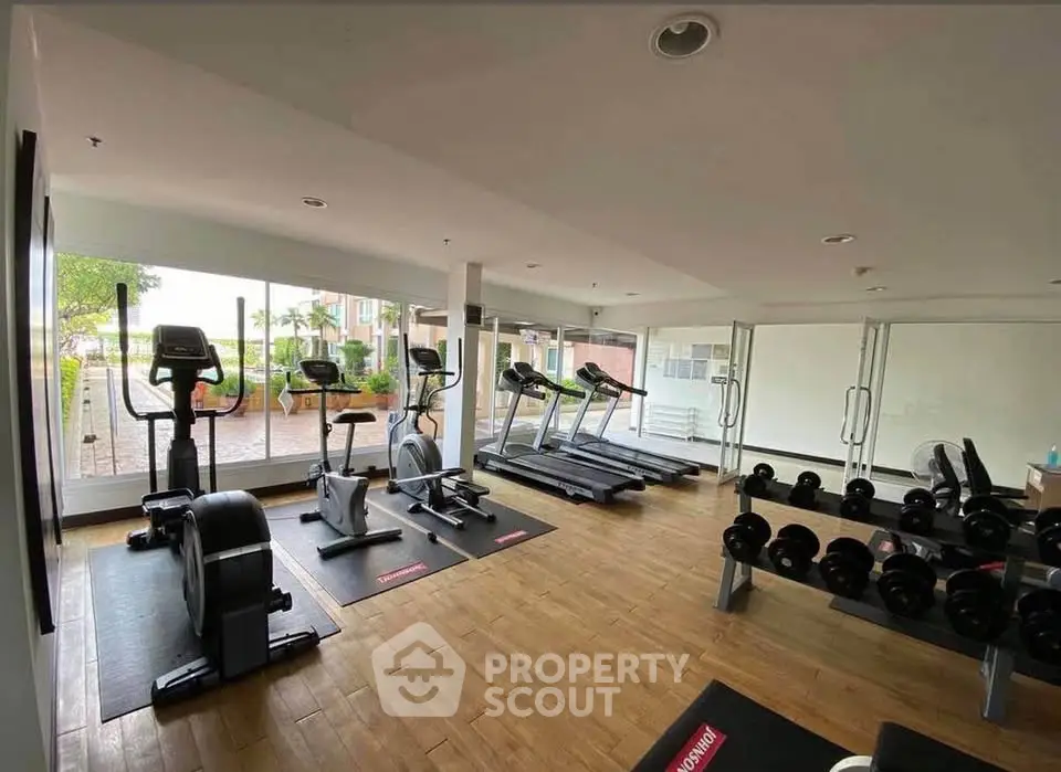 Modern gym with cardio and weight equipment in a bright, spacious room with large windows.