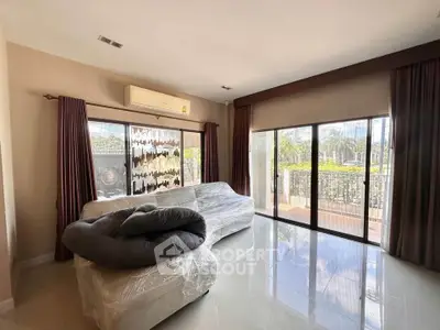 Spacious living room with large windows and balcony access, featuring modern furniture and natural light.