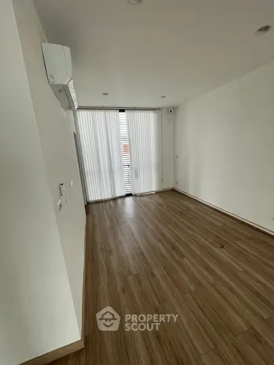 Spacious empty room with wooden flooring and large window, ideal for customization.