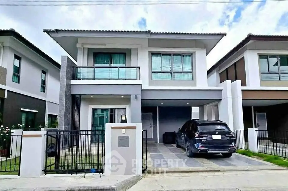 Modern two-story house with driveway and car parked, featuring sleek architectural design and large windows.