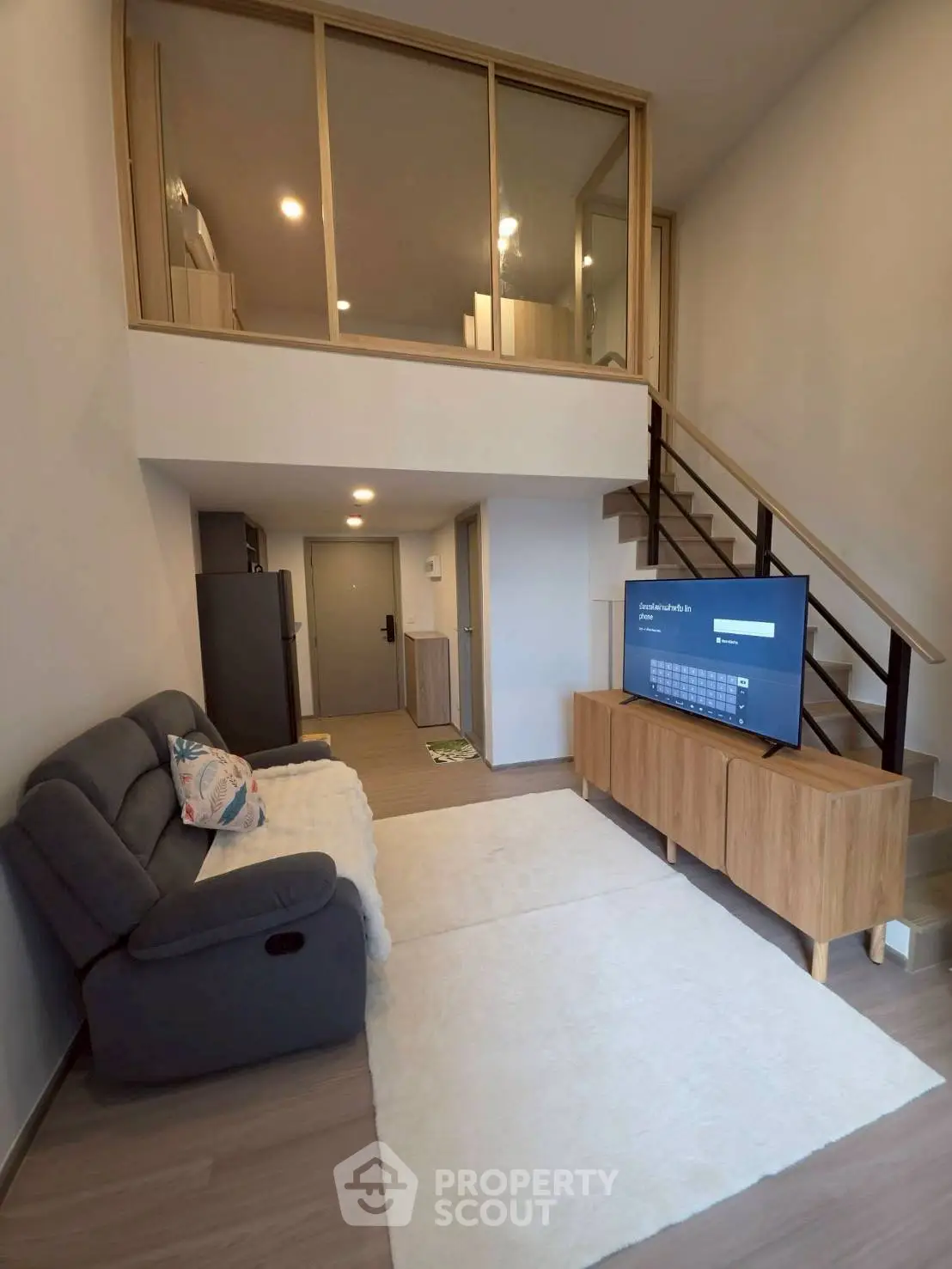 Modern loft-style living room with cozy sofa and large TV, featuring a mezzanine level and stylish decor.