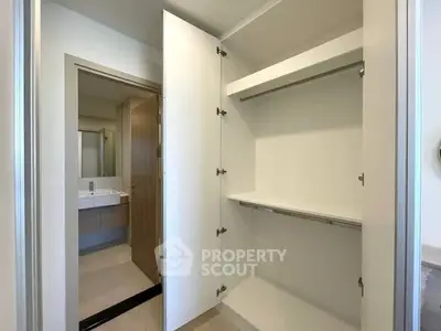 Spacious modern closet with open doors next to a sleek bathroom view.