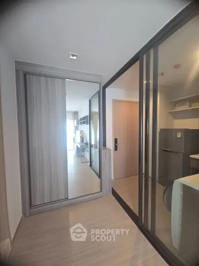 Modern apartment hallway with sliding glass doors and mirrored closet, leading to a bright living area.