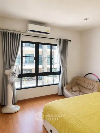 Bright bedroom with large window, cozy seating, and air conditioning in modern apartment.
