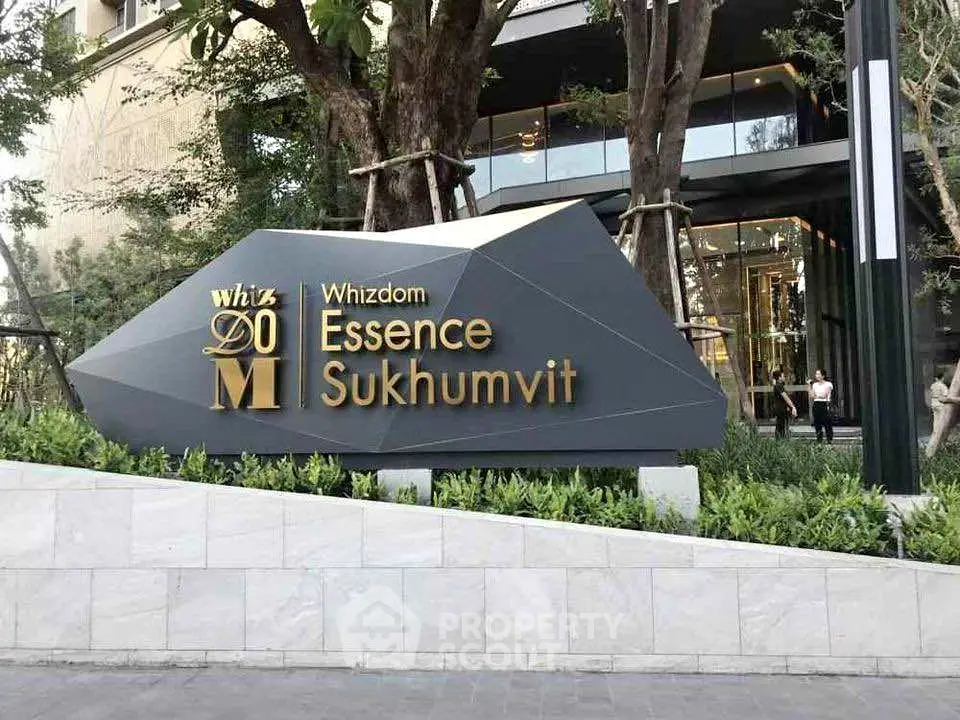 Modern entrance of Whizdom Essence Sukhumvit with sleek signage and lush greenery.