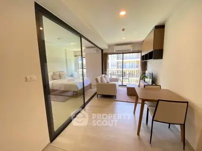 Modern open-plan living room with glass partition and cozy bedroom view.