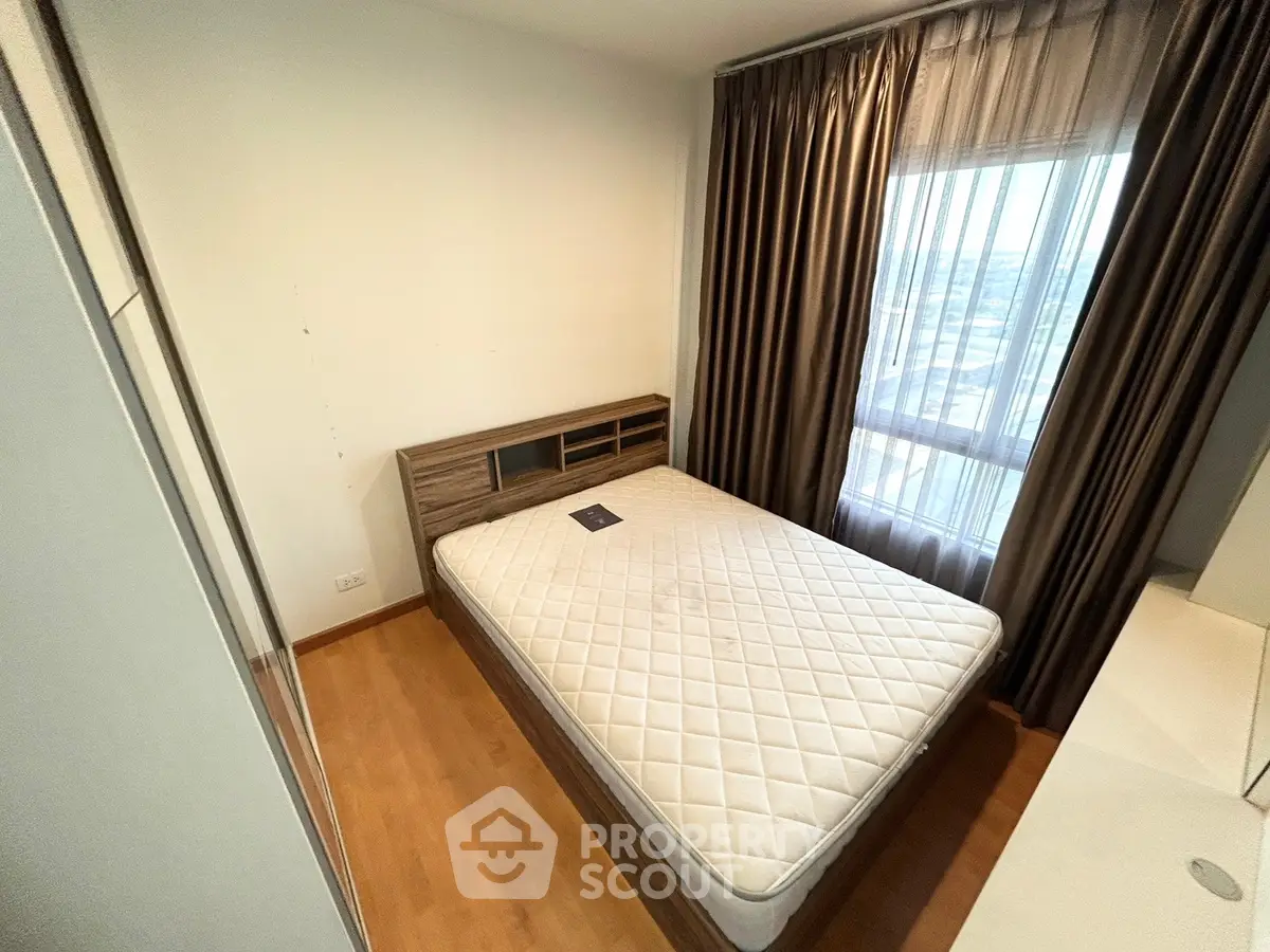 Cozy bedroom with large window and wooden flooring, perfect for relaxation.
