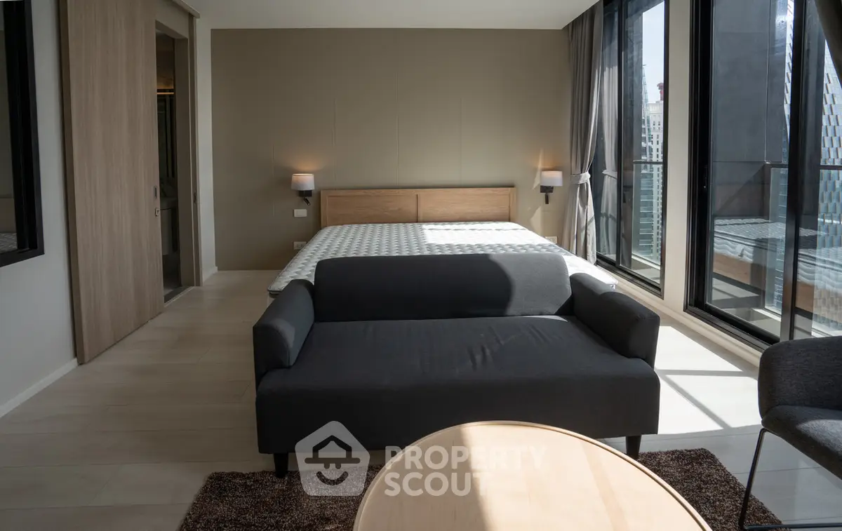 Modern bedroom with large windows and city view, featuring a cozy sofa and stylish decor.