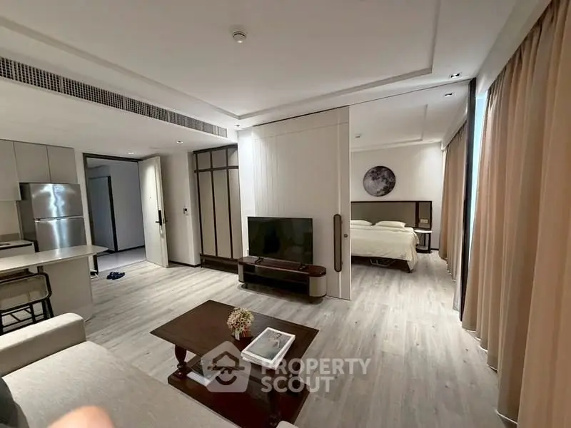Spacious open-plan living room with modern kitchen and cozy bedroom in a stylish apartment.