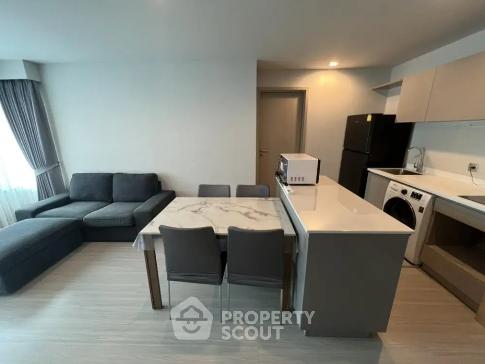 Modern open-plan living room with kitchen and dining area, featuring sleek furniture and appliances.