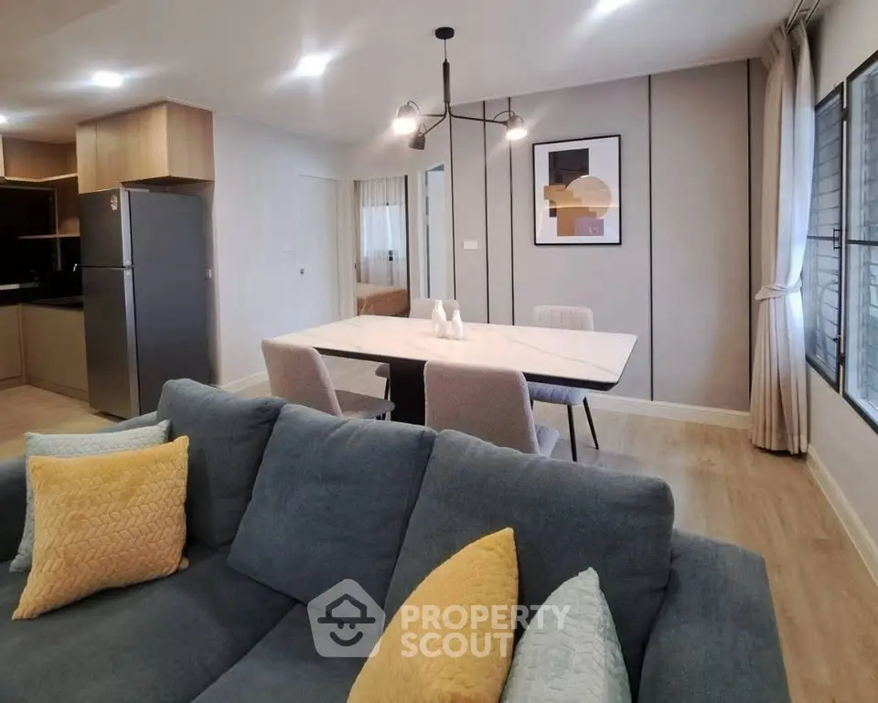 Modern living room with stylish decor and open dining area, featuring a cozy blue sofa and elegant lighting.