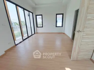 Spacious empty room with large windows and wooden flooring in modern home.