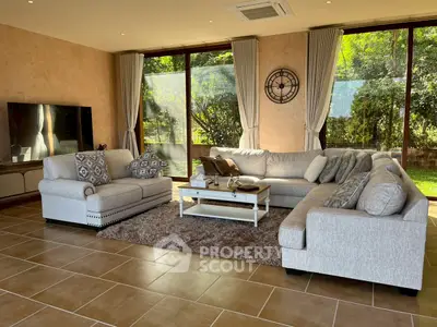 Spacious living room with elegant sofas and large windows overlooking a lush garden, perfect for relaxation.
