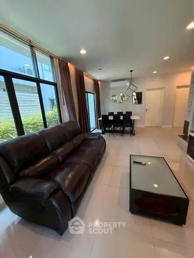 Spacious modern living room with leather sofa and dining area, featuring large windows and elegant decor.