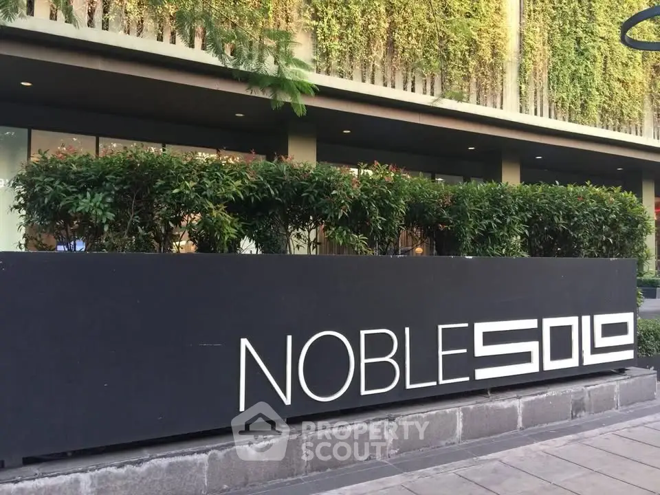 Modern building entrance with lush greenery and stylish signage at Noble Solo.