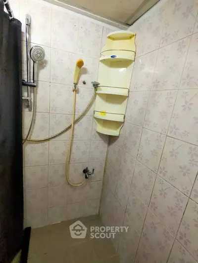 Compact bathroom with shower and tiled walls, featuring a corner shelf for storage.