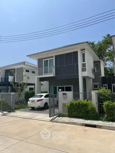 Modern two-story house with gated driveway and car parked in front, showcasing contemporary architecture.