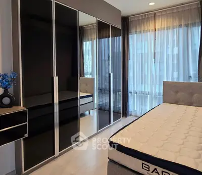 Modern bedroom with sleek black wardrobe and large windows for natural light.
