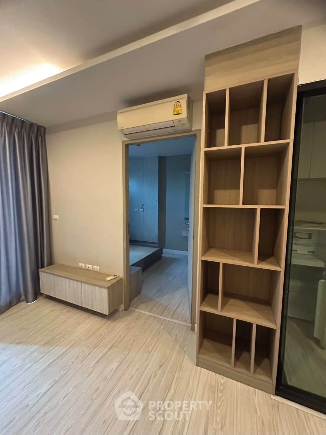 Modern apartment interior with sleek wooden flooring and built-in shelving, featuring an air conditioning unit.