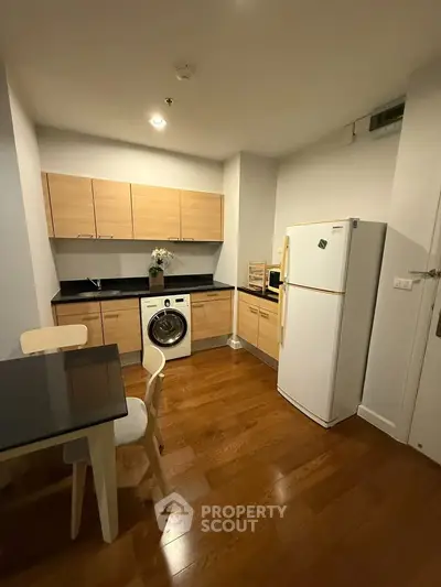 Modern kitchen with wooden cabinets, washing machine, and fridge in cozy apartment.