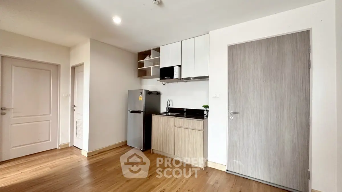 Modern compact kitchen with sleek cabinetry and stainless steel fridge in cozy apartment.