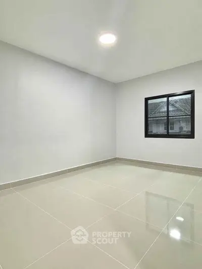 Spacious empty room with tiled flooring and large window, ideal for customization.