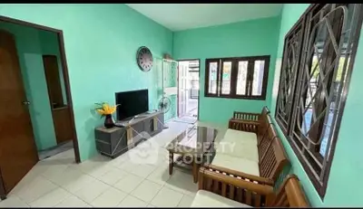 Charming living room with wooden furniture and TV, bright walls, and natural light.