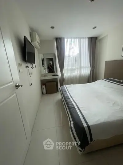 Cozy bedroom with modern decor, featuring a wall-mounted TV and large window for natural light.