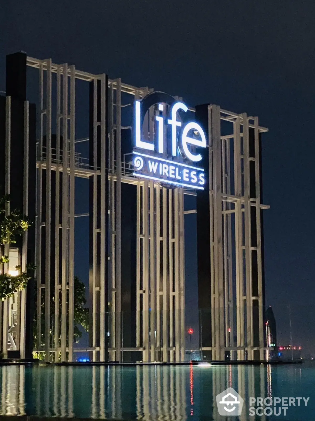 Modern architectural structure with illuminated signage by a serene poolside at night.