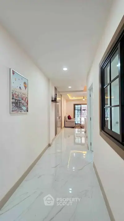 Bright hallway leading to a cozy living room with modern decor and large window.