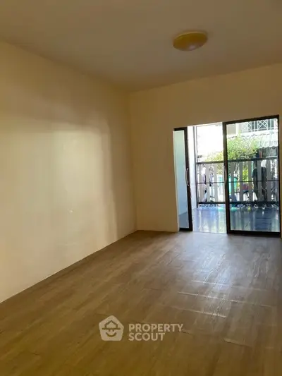 Spacious empty room with wooden flooring and sliding glass doors leading to a balcony.