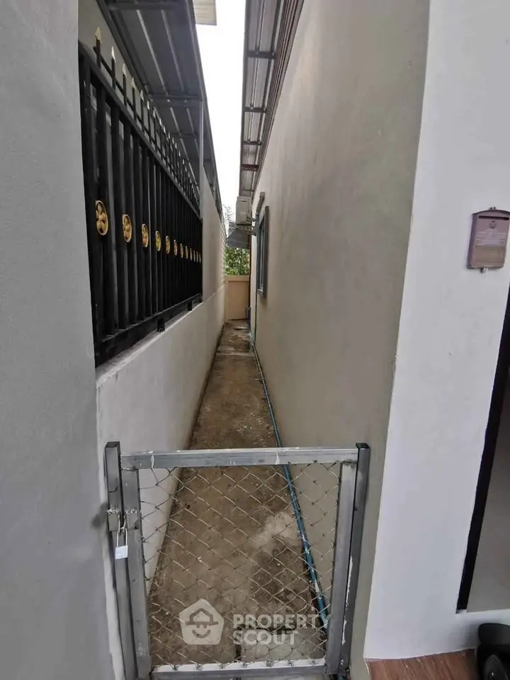 Narrow side alley with metal gate and concrete path between buildings.