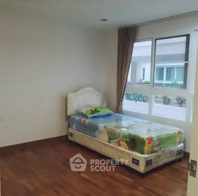 Spacious bedroom with single bed and large window offering natural light in modern apartment.