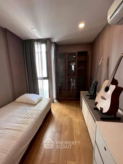 Cozy bedroom with wooden flooring and guitars, perfect for music lovers.