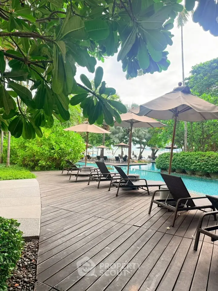 Luxurious poolside area with sun loungers and umbrellas surrounded by lush greenery, perfect for relaxation.