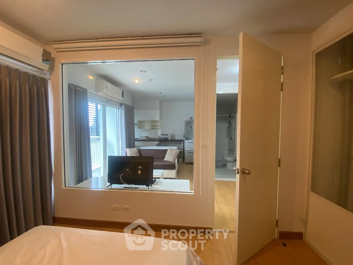 Modern apartment interior with open layout, featuring a cozy living room and kitchen view from bedroom.
