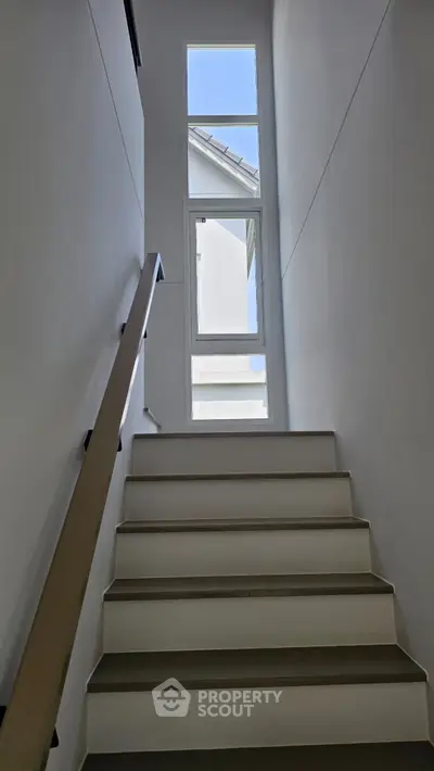 Modern staircase with large window offering natural light and architectural elegance.