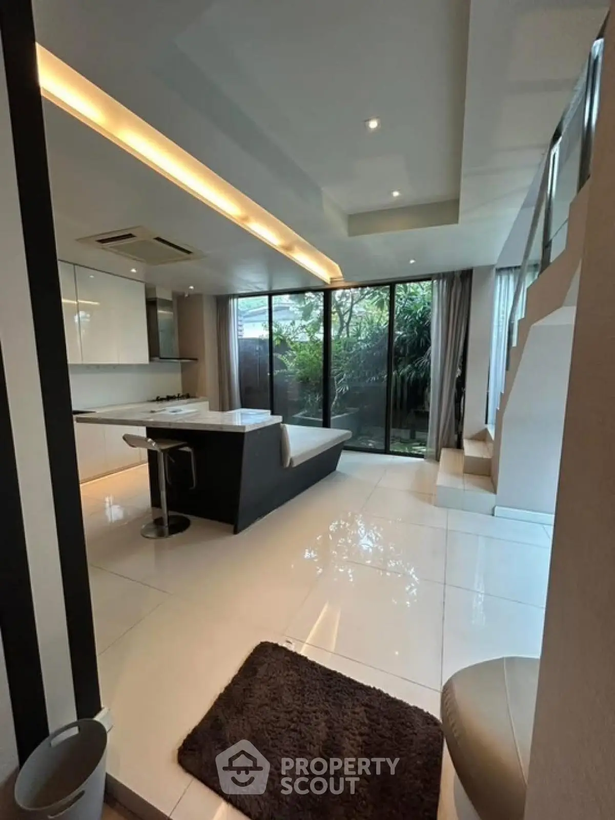 Modern open-plan living room with sleek kitchen and large windows overlooking greenery.