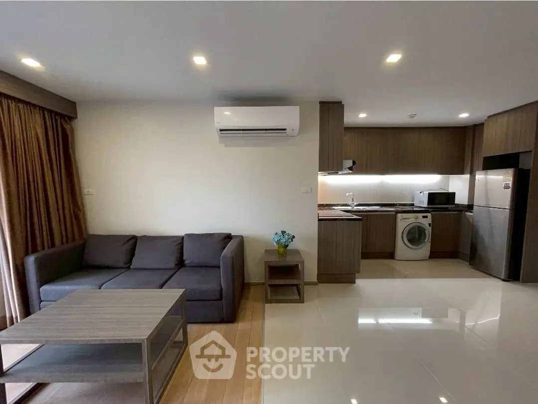 Modern living room with open kitchen, featuring sofa, air conditioning, and washing machine.