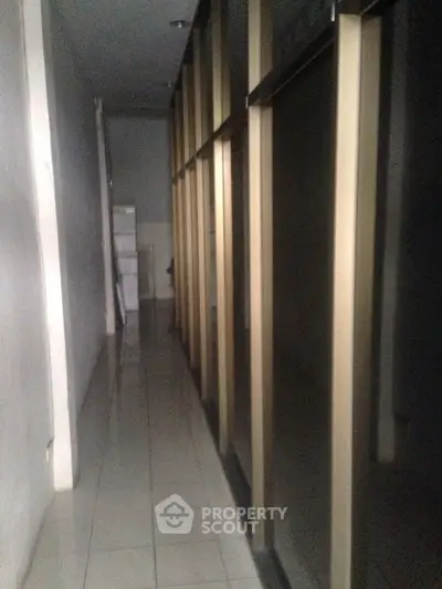 Narrow hallway with tiled floor and glass partitions in a commercial building.