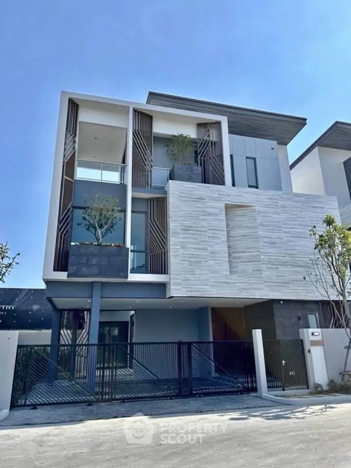 Modern three-story house with sleek design and large windows, featuring a gated entrance and stylish facade.