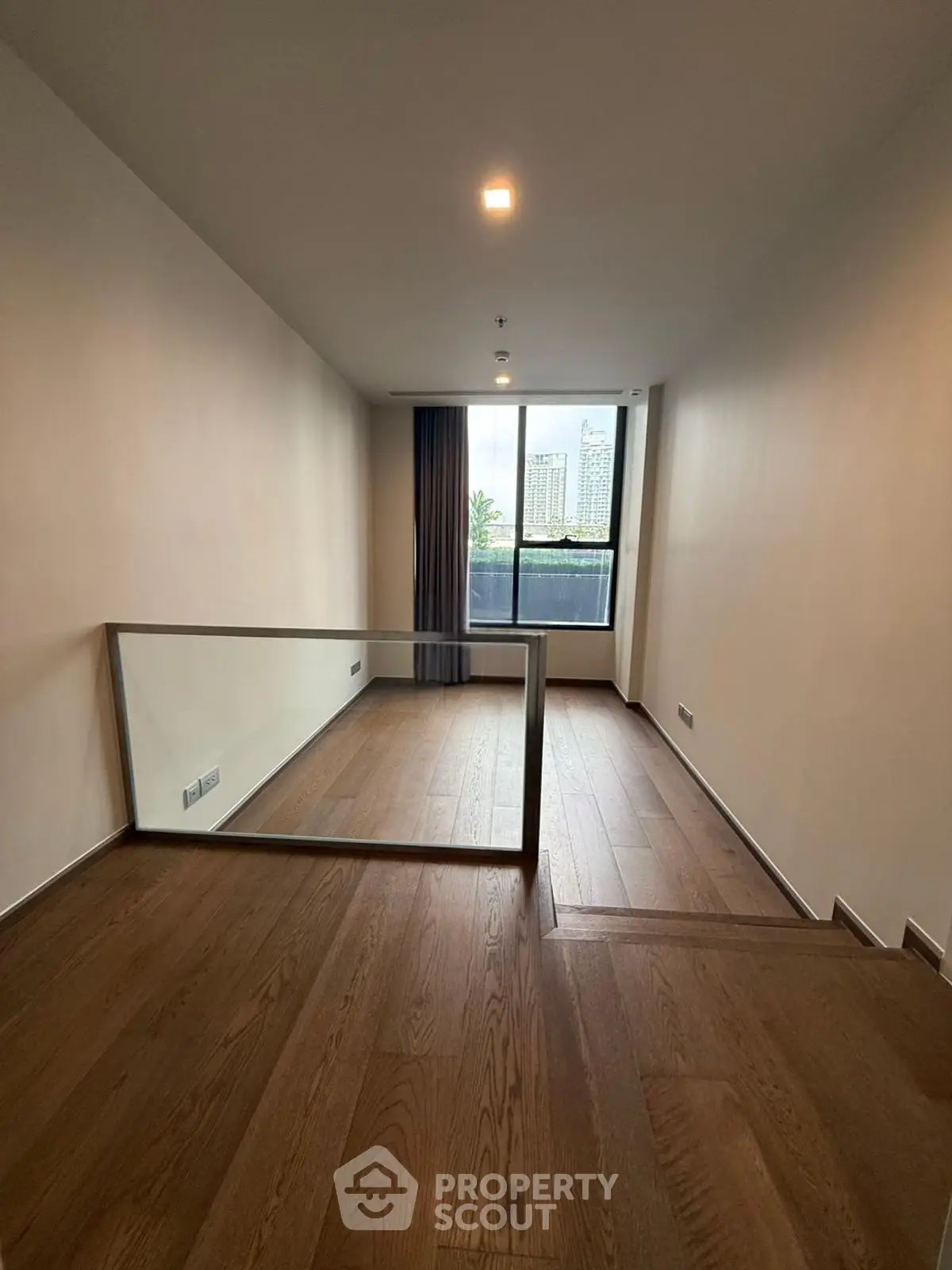 Spacious modern living room with wooden flooring and large window offering city views.