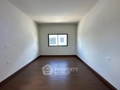 Spacious empty room with wooden flooring and large window, perfect for customization.