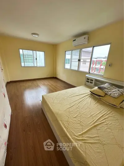 Spacious bedroom with wooden flooring and large windows in a modern apartment.