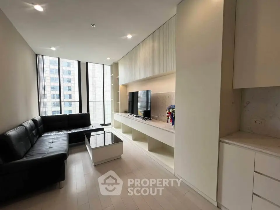 Modern living room with sleek black sofa and large windows in a high-rise apartment.