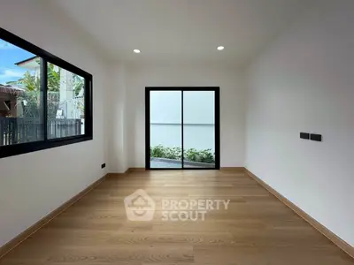 Spacious empty room with wooden flooring and large windows, perfect for customization.