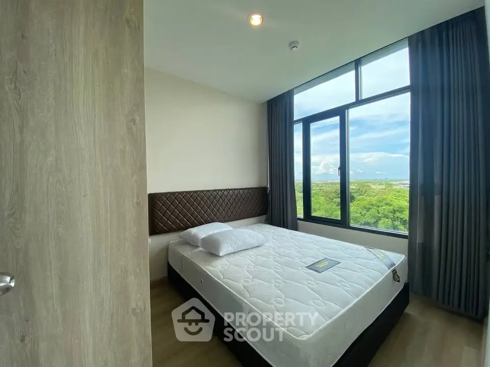Modern bedroom with large window offering stunning green view, featuring a comfortable bed and stylish decor.